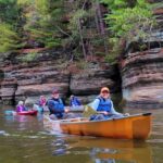 Image of canoeists paddling past sandstone bluffs.